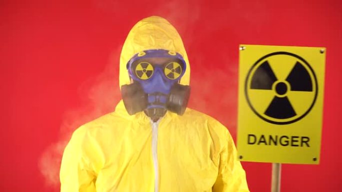 一个穿着防护化学服的男人，戴着防护面具，海报辐射着一对夫妇。隔离，工作室拍摄。红色背景上的辐射危害概