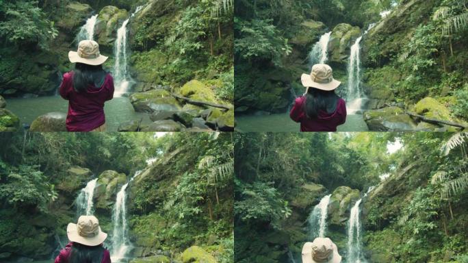 亚洲女性旅行者在热带森林中，有水流和落水的背景。自然旅行的概念。4k慢动作。