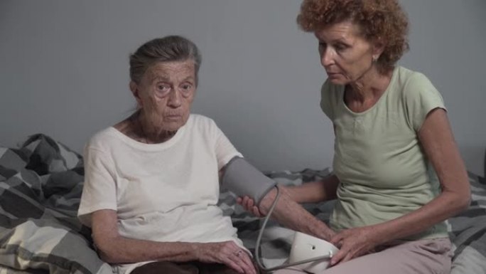 成熟的女性通过医疗家用电器血压计帮助高级女性测量血压。年迈的女儿正在照顾生病的老母亲。护士体检疾病高