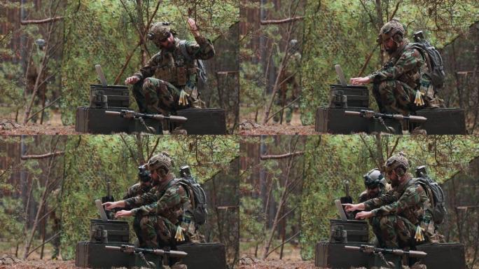 在一个临时森林基地里，一名留着胡子的指挥官身穿军装，身穿战术背心，头上戴着头盔，在笔记本电脑的键盘上