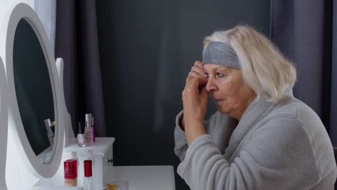老年老年妇女祖母涂抹抗皱眼罩，在家化妆