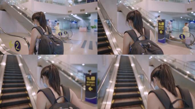 年轻的亚洲妇女戴口罩踩在自动扶梯上，从后面看，预防传染病，机场航站楼内，旅行风险，社交距离，新常态，