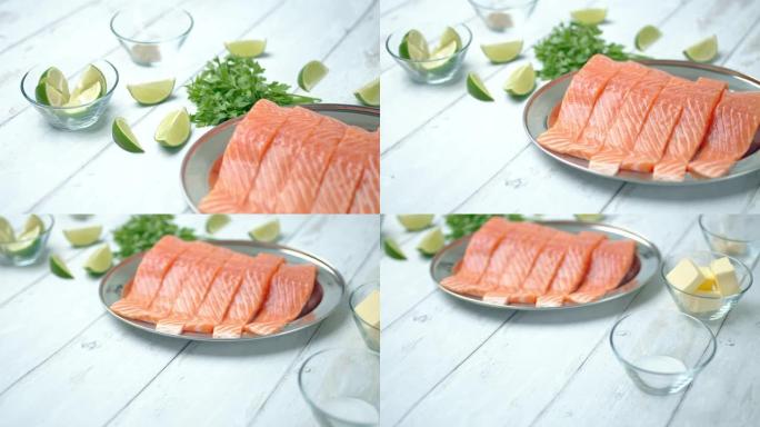 新鲜生红三文鱼切片的特写镜头。生三文鱼放在木制桌子上的银盘里，旁边有柠檬和香草/绿色成分。健康海鲜的
