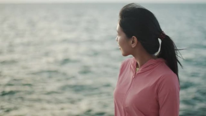 一位年轻的亚洲妇女的特写肖像，放松享受宁静的日落，仰望呼吸新鲜空气，在美丽的海景上放松。