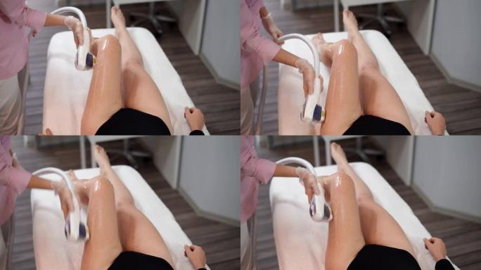 迷人的女性美容师做激光脱毛苗条的腿美丽的年轻女子是躺在一个美容沙龙的医疗沙发上。宇宙学，脱毛和水疗概
