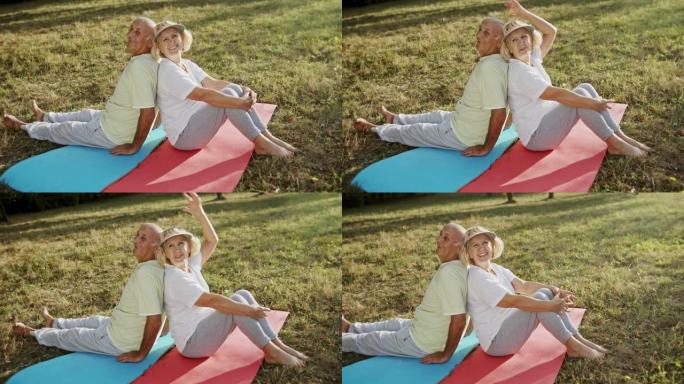 在公园健身锻炼休息时，开朗的老年男女背靠背坐在垫子上并互相交谈的高角度