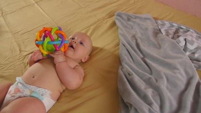微笑的婴儿躺在床单上的床上，用手握着玩具。儿童的感觉发育。特写镜头。