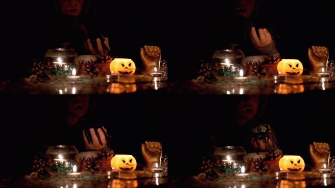 万圣节，戴兜帽的吸血鬼男孩在黑暗的房间里用蜡烛和蜘蛛玩耍