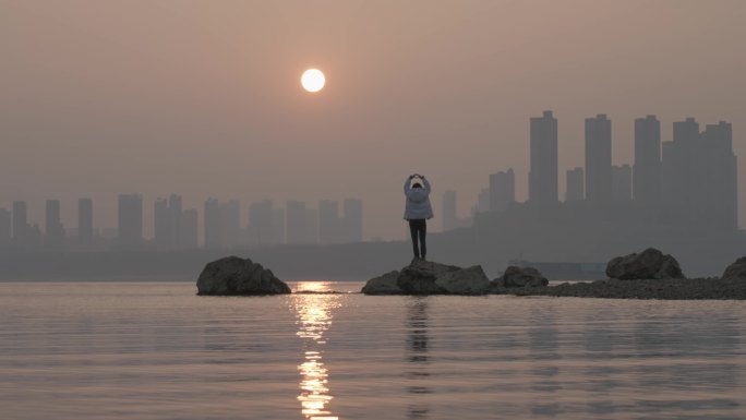 女生走上长江中的礁石跟夕阳互动打招呼