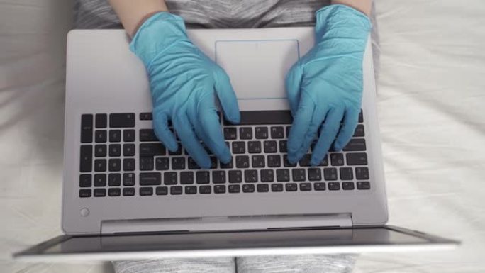 经理在家工作-使用笔记本电脑回答客户的问题。戴着口罩和手套在笔记本电脑上工作的女人