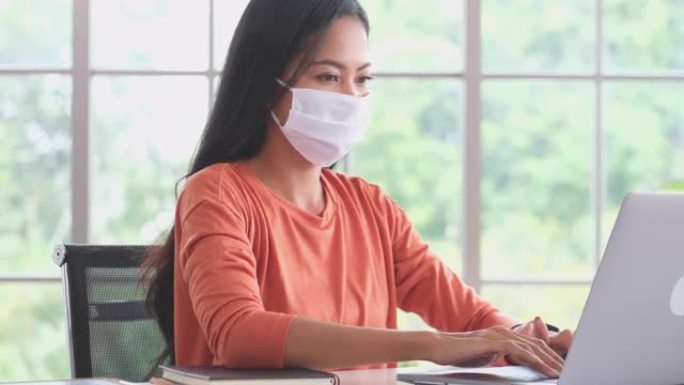 年轻的亚洲妇女在家里工作时戴着防护口罩防止病毒，防止空气中感染，冠状病毒概念，4k分辨率