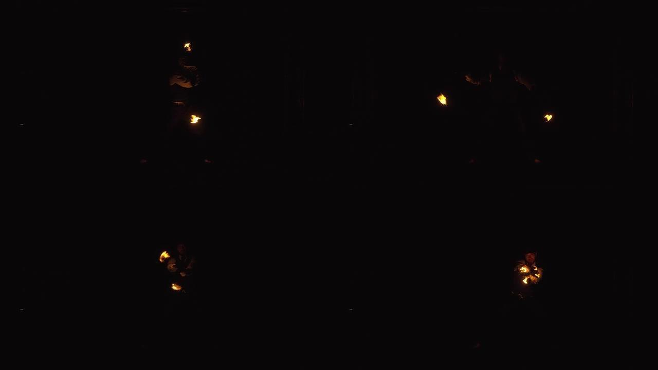 在黑暗中，可以看到一个人的轮廓在铁链上旋转着燃烧的火球，站在雨滴中。晚上激动人心的消防表演。慢动作