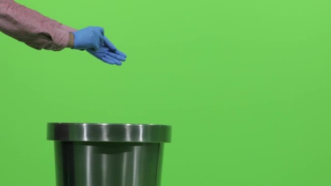一名男性双手取下绿色背景上的蓝色医用手套，取下手套并扔进垃圾桶。
