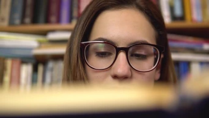 一名年轻女子正在图书馆看书。一个戴眼镜的女人仔细地看着书的特写。背景是书架上的书。图书图书馆。