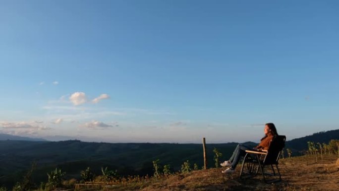 一位女性旅行者早上坐在山顶上看日出