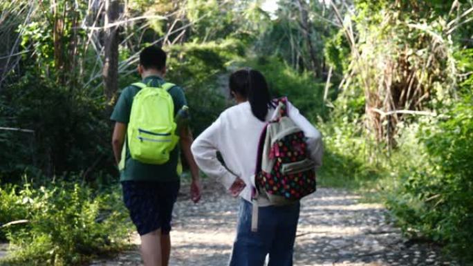 快乐的亚洲儿童带着背包在度假期间一起走在雨林中，户外冒险概念。