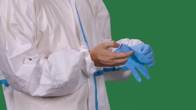 身穿白色防护服的男性医务人员戴上蓝色手术手套。躯干和手男人特写。绿色屏幕，色度键。慢动作