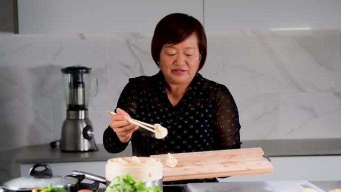 微笑的亚洲妇女打开一个竹蒸笼，用筷子将饺子移到木板上。中国传统烹饪概念。