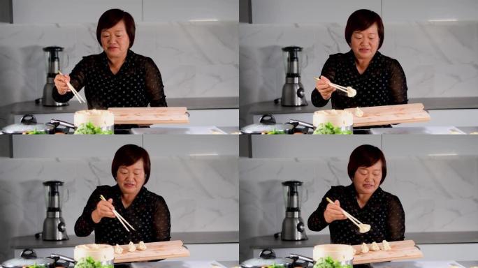 微笑的亚洲妇女打开一个竹蒸笼，用筷子将饺子移到木板上。中国传统烹饪概念。