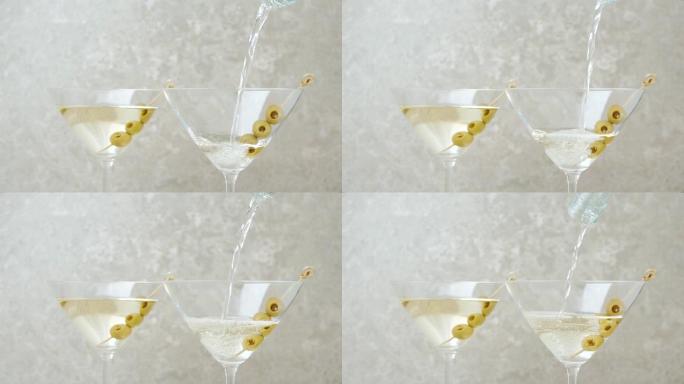 豪华马提尼酒。手将甜马提尼酒倒入空玻璃杯中，橄榄放在桌子上的棍子上，上面装饰着橄榄，鸡尾酒棒，石灰和