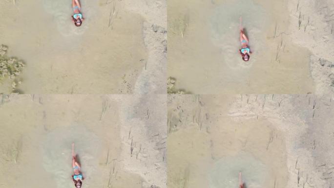 日光浴。一个穿着泳衣的女人在沙漠中间的一个小水坑里游泳。鸟瞰图