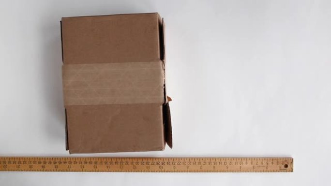 在准备运输时，用透明胶带绑扎送货箱。木质标尺放在包裹旁边的白色表面上