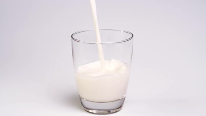 将牛奶倒入白色背景的玻璃杯中。