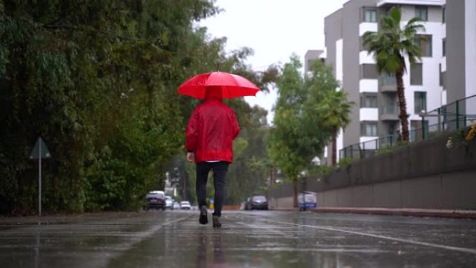 男子身穿红色雨衣，手持雨伞走在街上