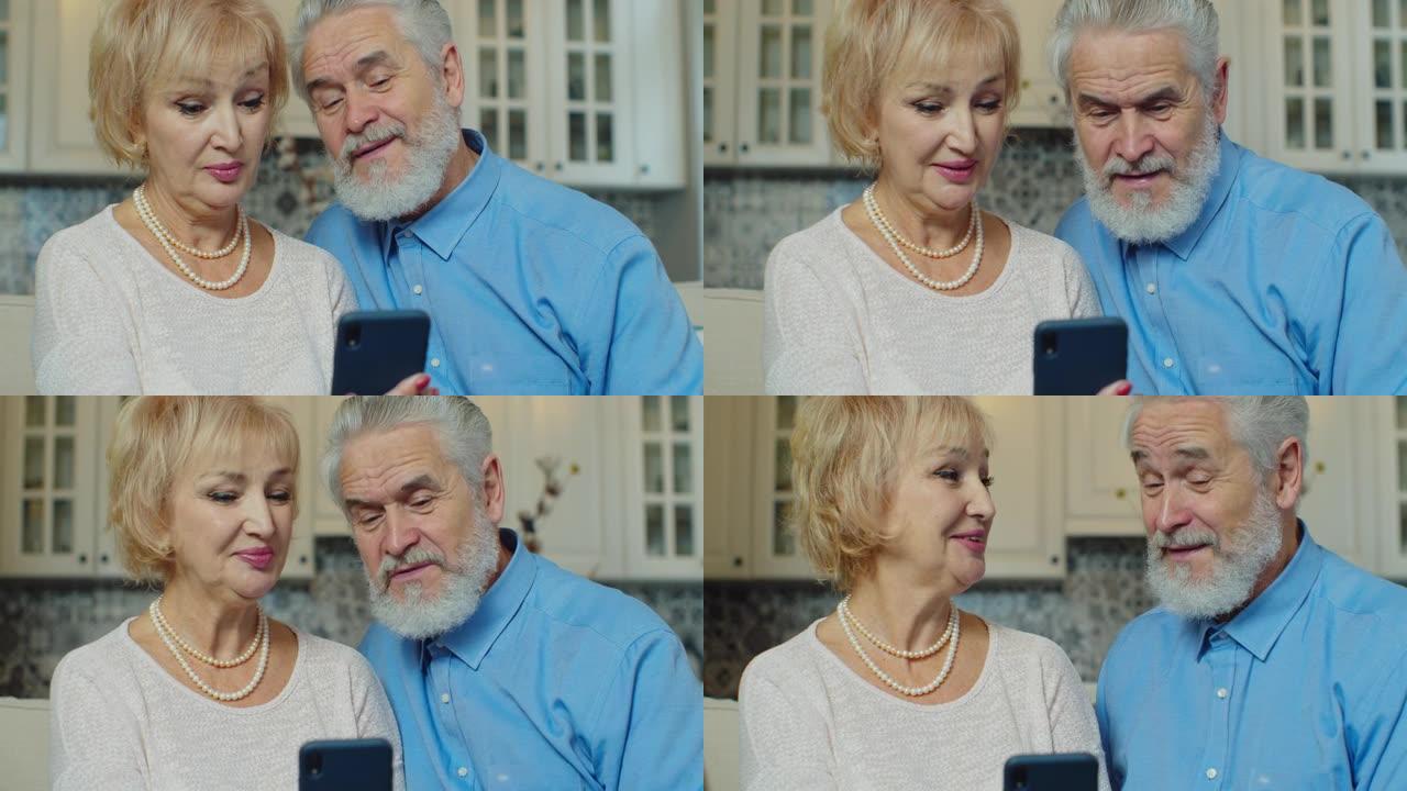 积极的祖母和祖父在智能手机上在线通话视频。微笑的老年人通过视频聊天交谈的肖像。使用智能手机的快乐老家
