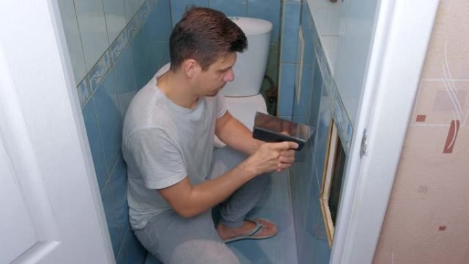 Man tiler在家中进行翻新维修，从厕所的墙壁上取下瓷砖。