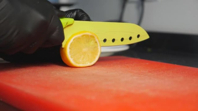 戴着手套的厨师的男性手臂在菜板上用刀在菜板上切新鲜的柠檬。厨师的手臂在厨房餐厅的塑料表面上切成柑橘类