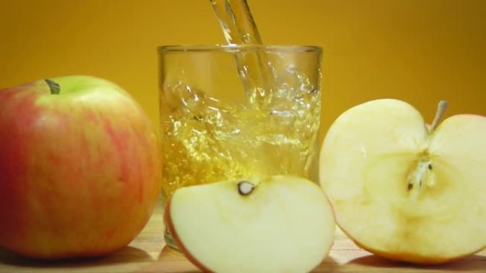 将新鲜的苹果汁倒入慢动作的黄色背景上的玻璃杯中