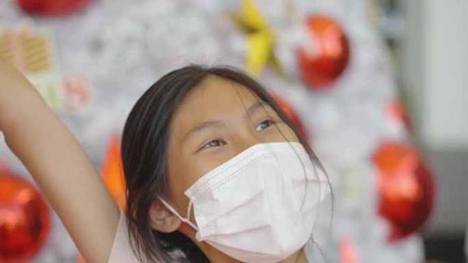 快乐的亚洲女孩戴着口罩，用圣诞树背景拍照或自拍，假期概念。