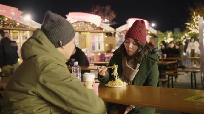 冬天晚上，亚洲夫妇坐在圣诞市场上的圣诞树附近。