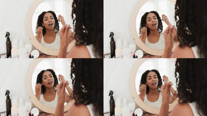 年轻的非洲裔美国妇女坐在镜子前，用牙线在浴室刷牙，后视图