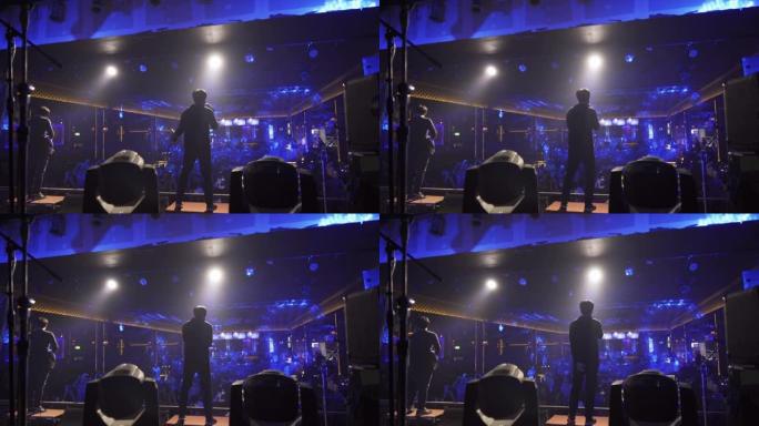 一位歌手与音乐乐队一起在disco pub club酒吧的舞台音乐会上表演，并带有照明激光束聚光灯表