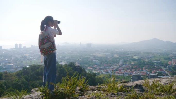 亚洲女孩使用双筒望远镜在山顶与蓝天的早晨，户外冒险的概念。