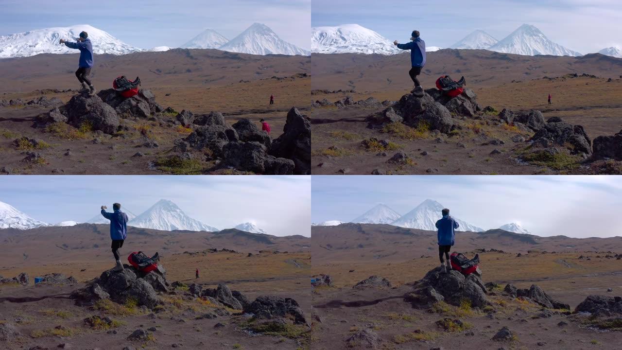 一位背着大背包的疯狂游客正在拍摄他的玩具鱼在堪察加半岛的山脉和火山中游泳。