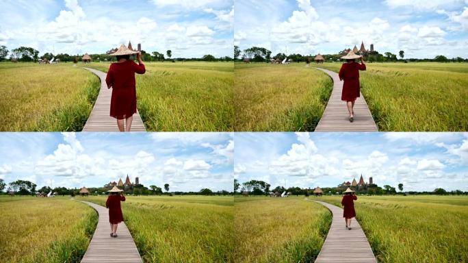 在稻田和Wat Tham Sua视图中，戴着草帽的成年妇女在木路上行走