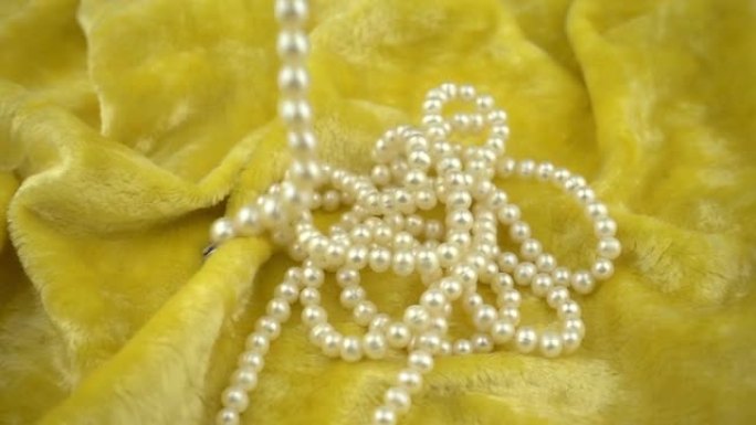 落在黄色天鹅绒柔软织物上的珍珠首饰在慢动作中。