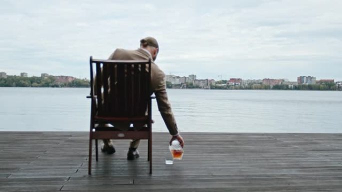 孤独的商人坐在海滨俯瞰城市，一边抽雪茄，一边喝浓烈的威士忌