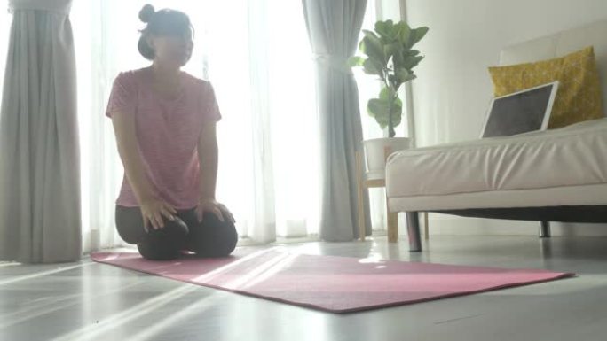 亚洲女性通过数字平板电脑在粉红色瑜伽垫上学习瑜伽，早晨在阳光照射下靠窗，在家中健康的生活方式理念。