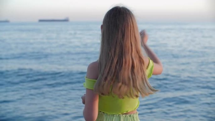 浪漫的女孩少年在船上风景从海岸向海水投掷石块。旅游女孩从岸上向大海扔石头，而地平线背景上五颜六色的日