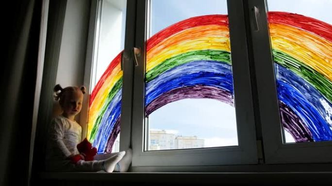 小女孩在窗户上画彩虹的背景。孩子们在家里休闲。居家隔离期间的积极视觉支持