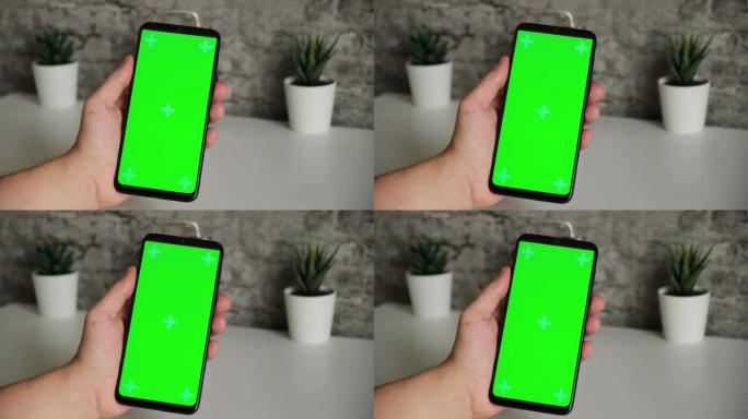 一个坐在白色办公桌前的男人手里拿着手机，屏幕上是绿色的。在智能手机的chromakey屏幕上滑动并点