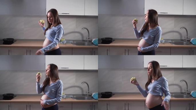 孕妇在厨房跳舞。吃一个青苹果有趣的手动作和好心情。复制空间。