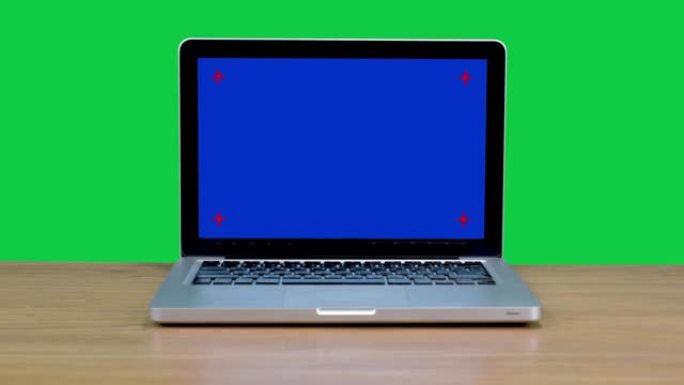 蓝屏笔记本电脑坐在木桌上，色键绿色屏幕背景。在家工作的概念。