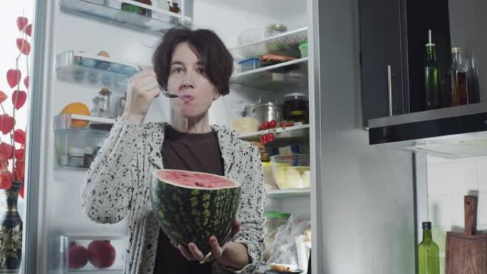 成熟的女人在冰箱旁边吃西瓜