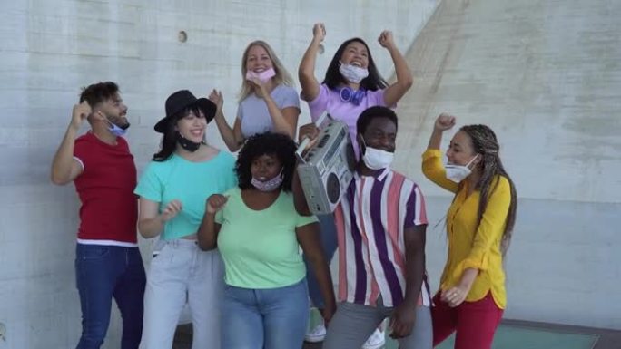戴着口罩的快乐朋友在老式音箱户外听音乐 -- 多种族年轻人在科罗纳病毒爆发期间一起跳舞很开心