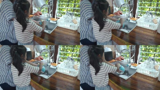 亚洲女孩和她的母亲在家里的厨房里一起吃完饭后，帮助清理和清洗餐具。